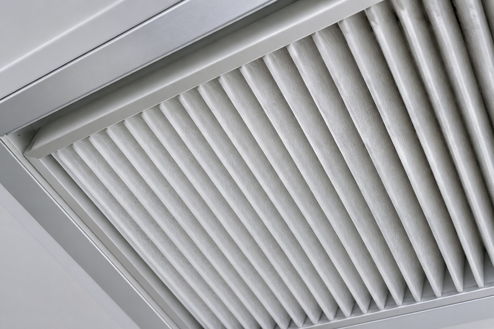 Macro of a HEPA filter pleated grille in a cleanroom ceiling, one-point light raking across the pleats